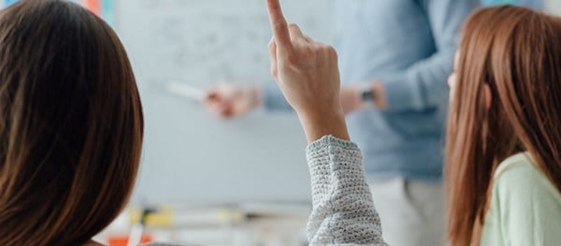 Young researcher giving a lecture to a group of students, a student is raising her hand and asking a question